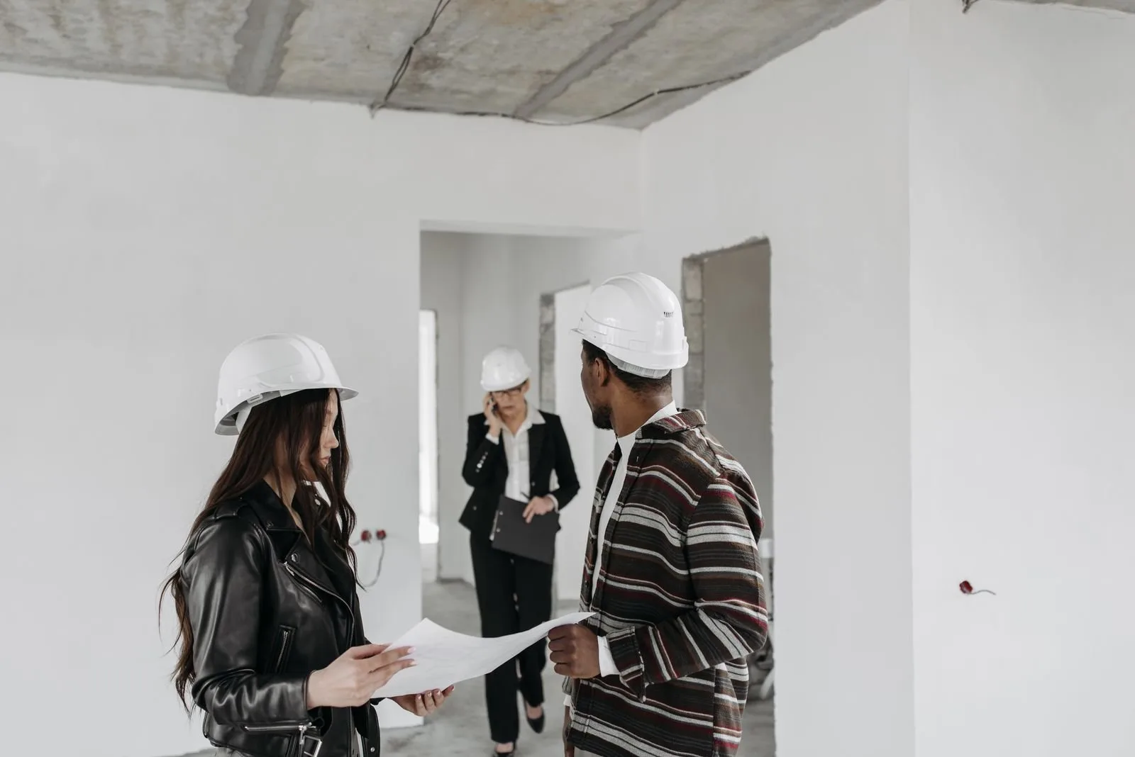 Equipo de servicios para el hogar con cascos revisando planos juntos en una obra
