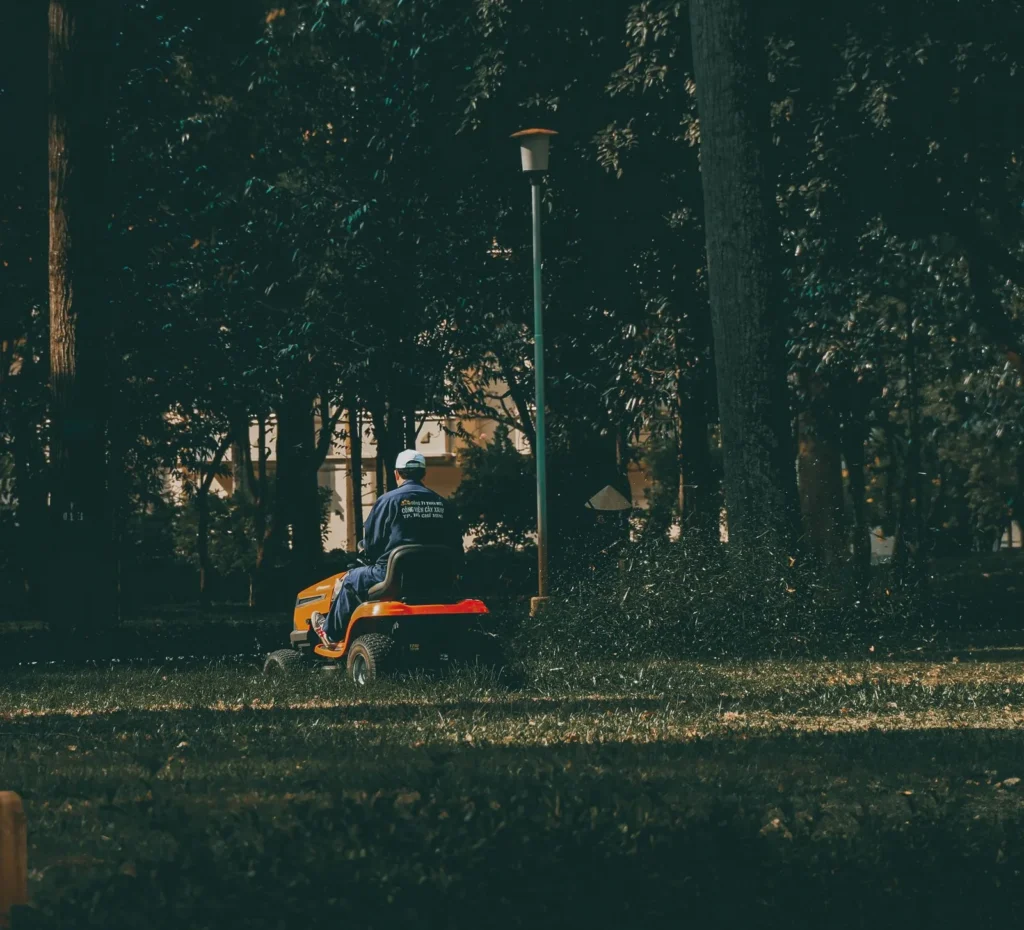 Landscaping marketing for maintenance crews: man in blue coveralls riding a lawn mower in a green park