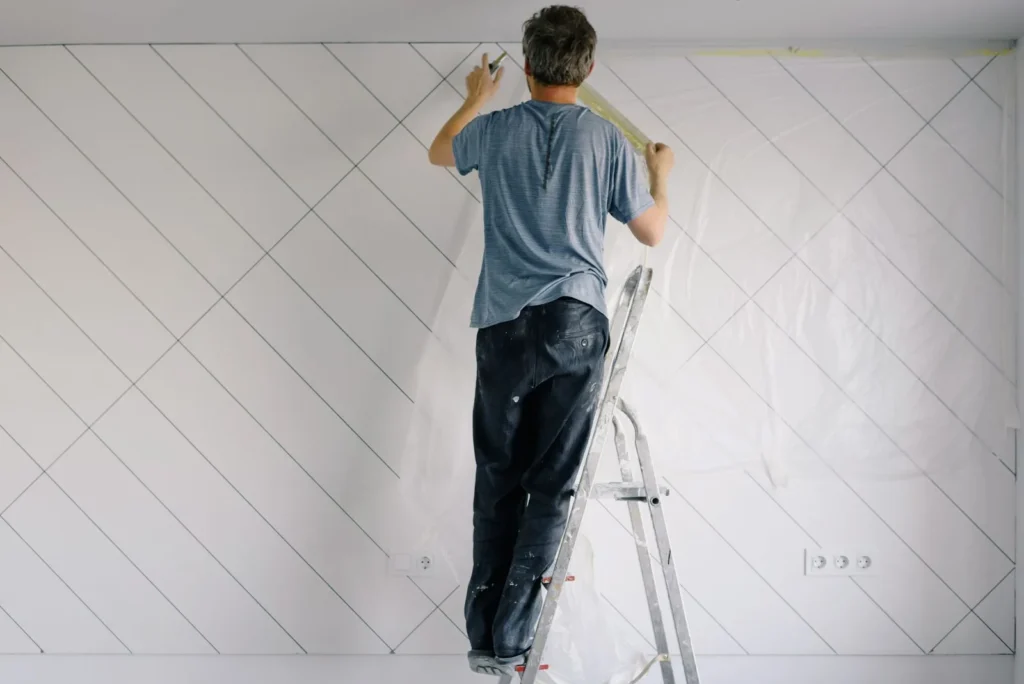 Painter on a ladder applying an undercoat to a wall in a bright, empty room