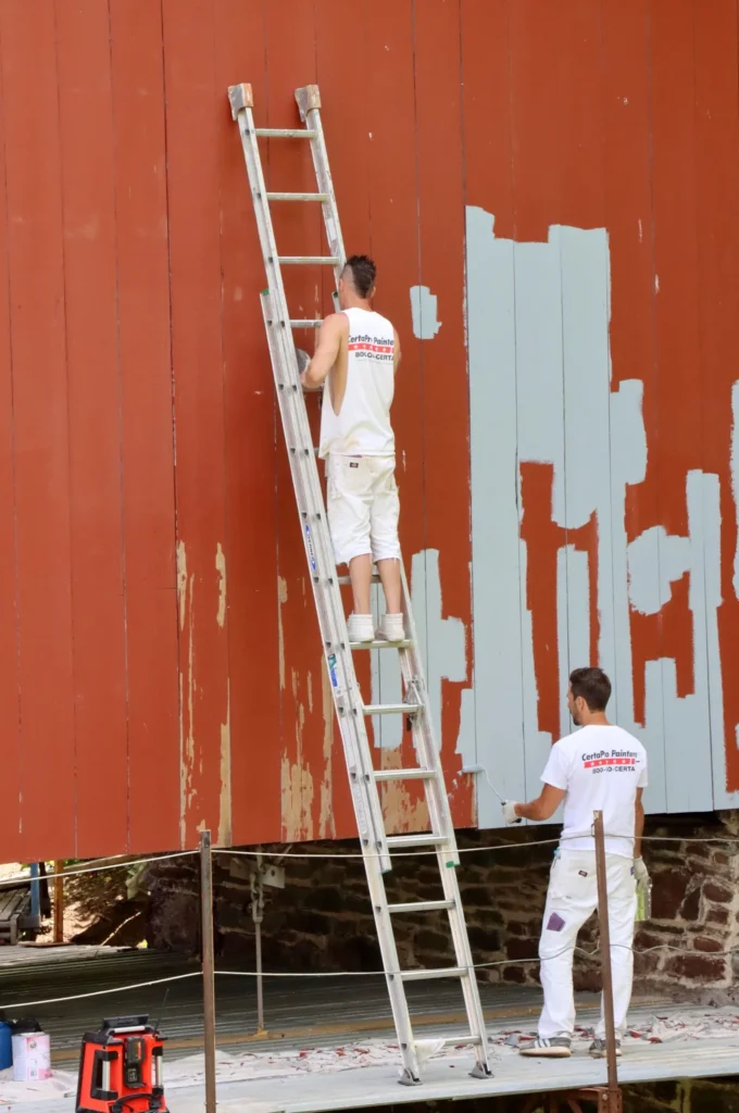 Painting contractor marketing: two painters in white uniforms using a ladder to repaint an exterior wooden wall