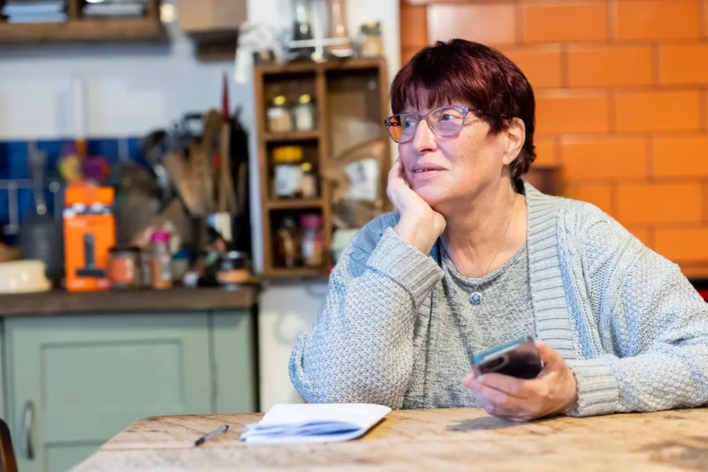 Woman at a kitchen table holding her smartphone while looking up an answer